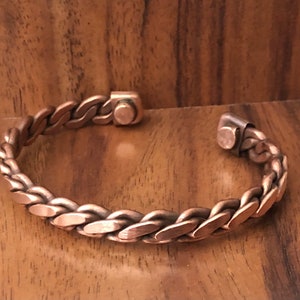 May include: A copper braided bracelet with magnetic clasps. The bracelet is made of a thick, woven copper wire.