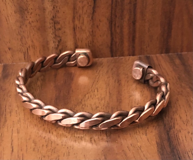 May include: A copper braided bracelet with magnetic clasps. The bracelet is made of a thick, woven copper wire.