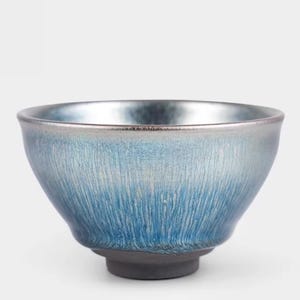 May include: A ceramic bowl with a metallic silver rim and a gradient blue glaze. The bowl's exterior features vertical textured lines, transitioning from a darker blue at the base to a lighter blue near the rim. The base is a dark gray color.