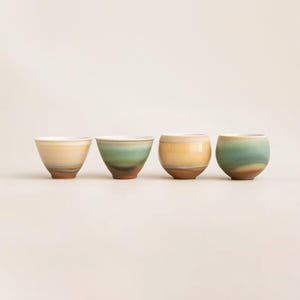 May include: Four handcrafted ceramic bowls with a unique design. Each bowl features a gradient of colors, including yellow, green, and blue, with a brown base. The bowls have a smooth, rounded shape, perfect for serving small portions of food or as decorative items.