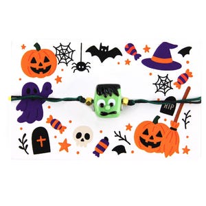 Op de afbeelding: Een Halloween-armband met een groene Frankenstein-monsterkraal, omringd door oranje pompoenen, paarse geesten en andere feestelijke decoraties. De armband is geregen op een groen koord en bevat goudkleurige kralen.