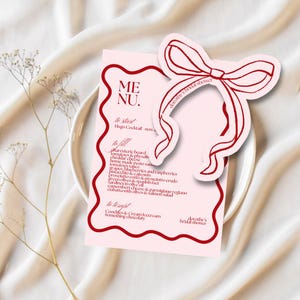 Pode incluir: Um cartão de menu rosa com uma borda vermelha e uma ilustração de laço vermelho. O cartão de menu lista um coquetel Hugo, uma tábua de charcutaria e sobremesas. O texto "dorothy's bridal shower" está escrito no cartão.