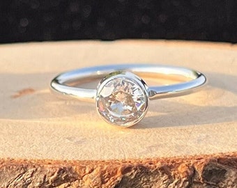 May include: A silver ring with a clear round gemstone set in a bezel setting.