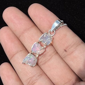 May include: A silver pendant necklace featuring three pink opal stones set in a silver frame.