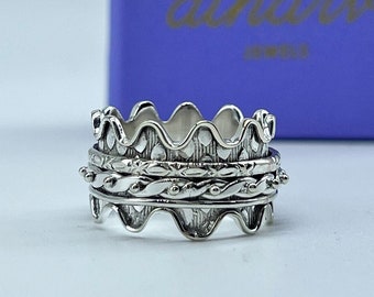 May include: A silver spinning ring with three bands. The top band has a wavy design, the middle band has a braided design, and the bottom band has a beaded design.