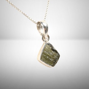 May include: A silver chain necklace with a pendant featuring a raw, green, faceted gemstone.