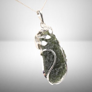Pode incluir: Um pingente de prata com uma pedra de moldavite verde engastada em um delicado design de folhas de prata.