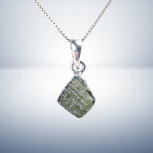 May include: A silver chain necklace with a pendant featuring a raw, green, faceted gemstone.