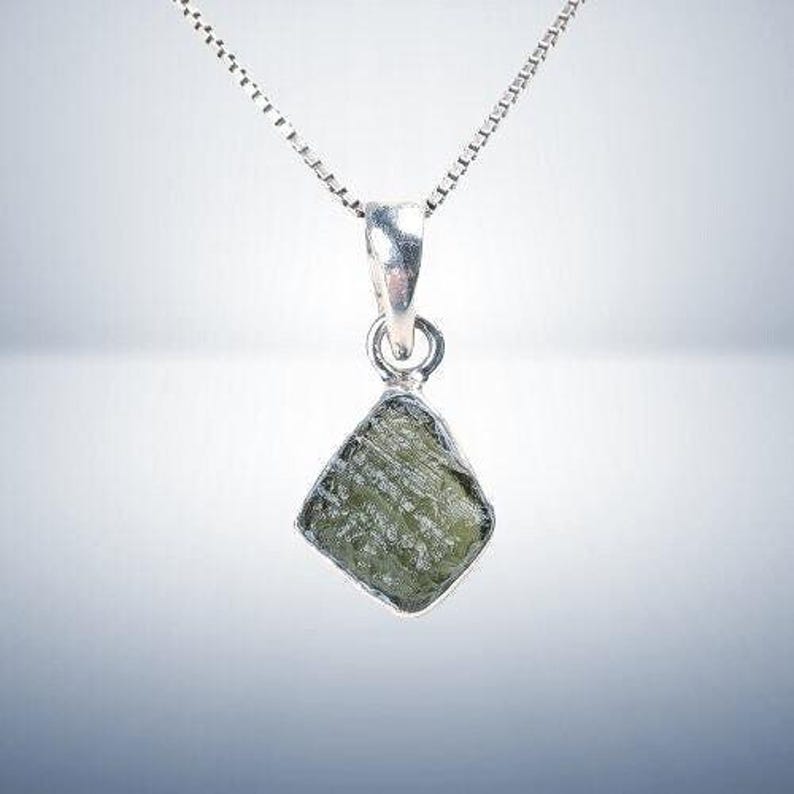 May include: A silver chain necklace with a pendant featuring a raw, green, faceted gemstone.