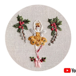 May include: Embroidered hoop art featuring a yellow and white ballerina with a red bow, surrounded by green holly sprigs with red berries.