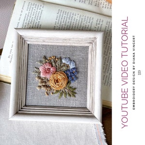May include: A framed embroidery design of a floral bouquet with pink, yellow, and blue flowers on a linen background. The frame is white with a distressed finish.