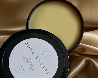 May include: A black jar with a white label that reads "SVRKHT HOME BODY BUTTE SHEA 8oz". The jar is filled with a light yellow body butter.