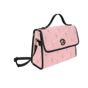 Puede incluir: Un bolso de mano rosa y negro con un patrón geométrico. El bolso tiene un asa superior y una correa larga para el hombro.