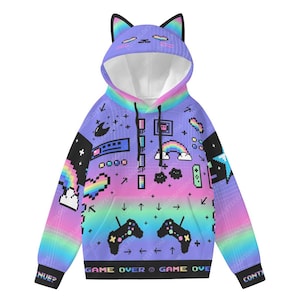 May include: A hooded sweatshirt with cat ear detailing. The design features pixelated graphics of rainbows, game controllers, and the text "GAME OVER". The colour scheme is a gradient of purple, blue, and pink.
