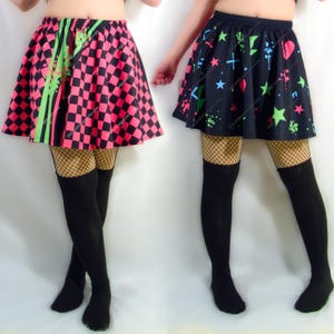 May include: Two skater skirts, one with a pink and black chequered pattern and neon green stripes, the other with a black background and colourful star and heart shapes. Both skirts are paired with fishnet stockings and black thigh-high socks.