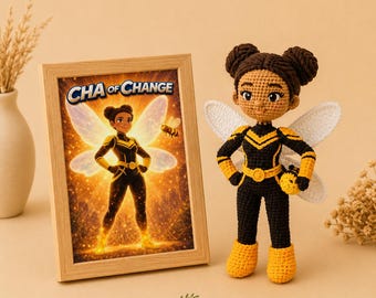 May include: A crochet doll featuring a character with dark brown hair in two buns, wearing a black and yellow superhero suit with white wings. Beside it is a framed print showing the same character with the text "CHA of CHANGE" above.