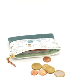 May include: A small teal zippered pouch with a white floral print and gold accents. The pouch is open and has a few euro coins spilling out.