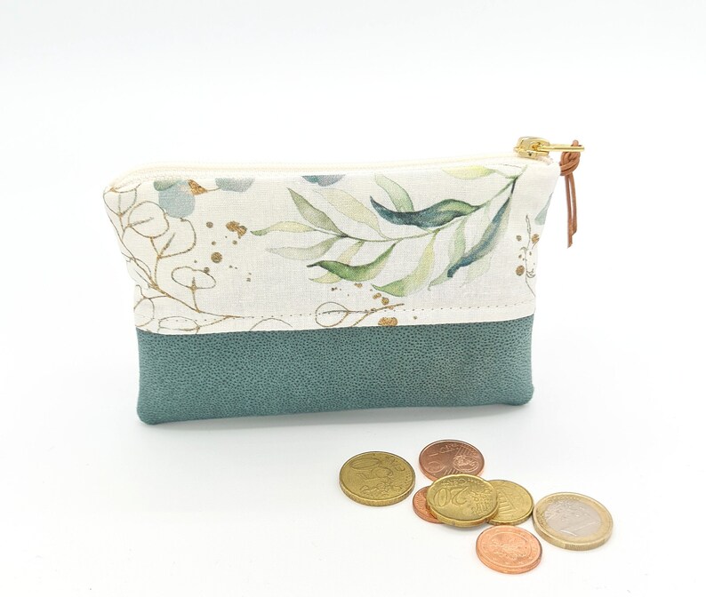 May include: A small, zippered pouch with a floral print on the top half and a solid teal bottom half. The pouch is made of fabric and has a gold zipper.