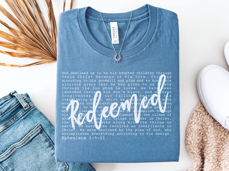 Christian women’s t shirt with the word Redeemed in white script lettering layered over Ephesians scripture text. Minimalist faith based tee with a soft, relaxed fit.