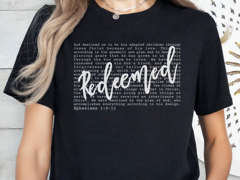 May include: Black t-shirt with the word "Redeemed" in a white script font. The shirt features a block of text in a smaller font, with the Bible verse Ephesians 1:5-11.