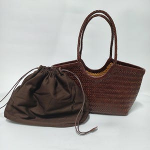 May include: A brown woven tote bag with braided handles and a matching drawstring pouch. The bag has a rectangular shape with a wide opening. The pouch is made of a soft, dark brown fabric.