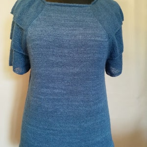 Op de afbeelding: Een blauw gebreid topje met een gerimpelde halslijn en korte mouwen.