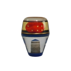 Puede incluir: Una perilla de cambio de marchas de acrílico transparente con un dado rojo en su interior. El dado tiene puntos dorados y flota en el líquido transparente. La perilla tiene una base azul.