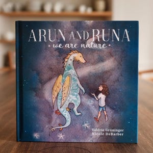 Könnte beinhalten: Ein blauer Buchumschlag mit dem Titel "Arun und Runa: Wir sind Natur". Der Umschlag zeigt eine Aquarell-Illustration eines gelben und blauen Drachen und eines Mädchens mit braunen Haaren.