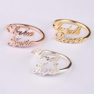 May include: Three gold rings with two names on each. The rings are in different colors: rose gold, gold, and silver. The names on the rings are "Sophia Kristina", "Michelle Donna", and "Wendy Kyle".