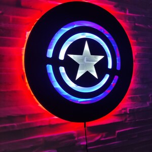 May include: A black circular wall light with a white star in the center and blue and red LED lights around the star. The light is mounted on a brick wall.