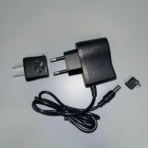 May include: A black power adapter with a black power cord and a black plug. The adapter has a European plug and a DC plug.