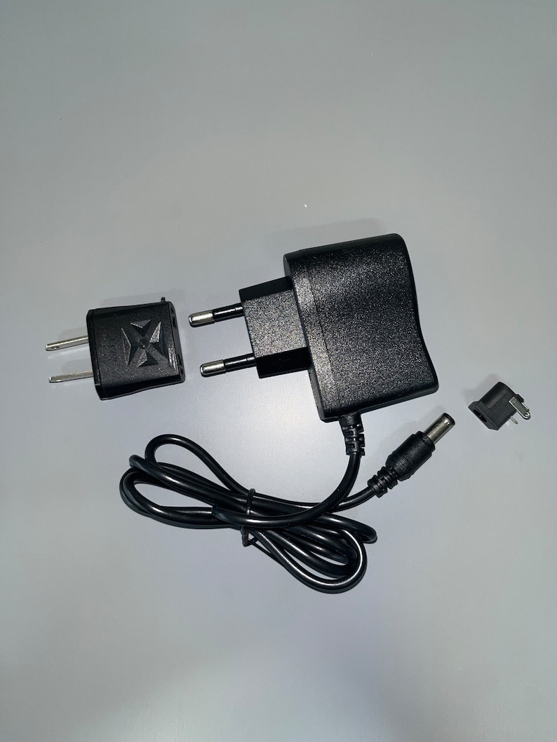 May include: A black power adapter with a black power cord and a black plug. The adapter has a European plug and a DC plug.