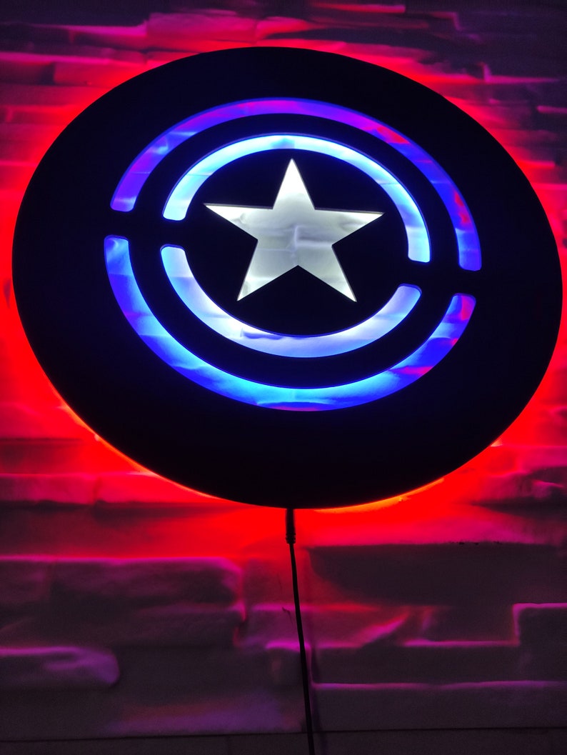 May include: A black circular wall light with a white star in the center. The light is surrounded by a blue and red ring. The light is on and illuminating the wall behind it.