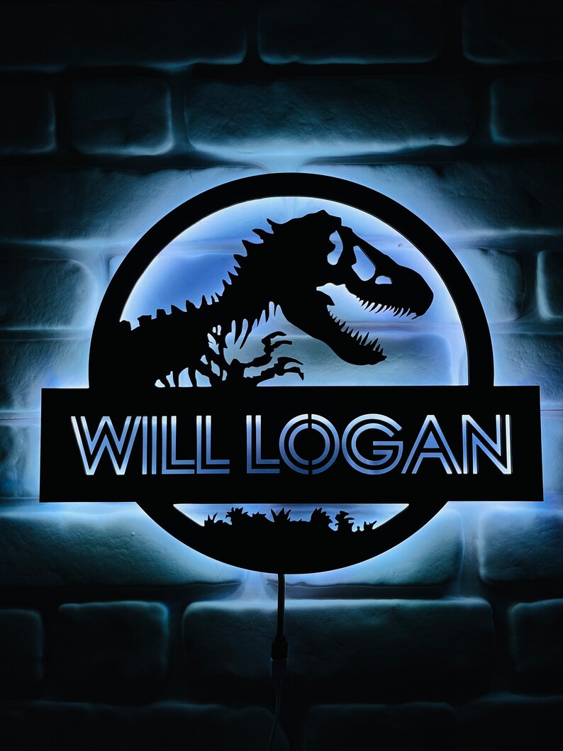May include: A black, illuminated sign featuring a dinosaur skeleton silhouette within a circular frame. The name "WILL LOGAN" is displayed in white, block letters below the circle. The sign is mounted on a brick wall with a blue glow.