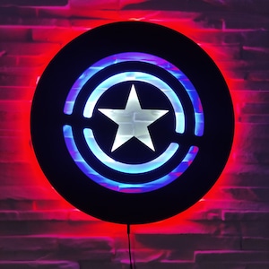 May include: A black circular wall light with a red and blue illuminated design. The design features a white star in the center surrounded by two concentric circles.