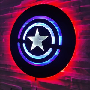 May include: A black circular wall light with a white star and blue and red concentric circles. The light is illuminated with red and blue LEDs.