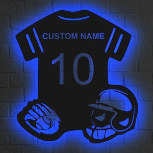 Pode incluir: Uma camisa de beisebol preta com o texto "CUSTOM NAME" e o número "10" na frente. Uma luva de beisebol e um capacete de beisebol estão na parte inferior da camisa.