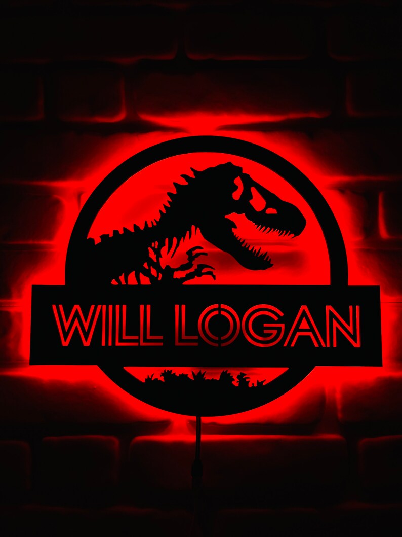 May include: A black illuminated sign with the name "WILL LOGAN" in red, featuring a dinosaur silhouette within a circular frame. The sign is mounted on a brick wall and emits a red glow.