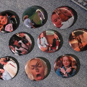 Op de afbeelding: Een verzameling van acht ronde speldjes met diverse fotografische scènes uit een film. Elke button toont een eigen afbeelding, waaronder personages in verschillende omgevingen, een zonsonderganglandschap en portretten van individuen.
