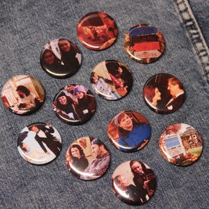 May include: A collection of 11 round buttons featuring images from the popular television show Gilmore Girls. The buttons feature various characters and scenes from the show, including Lorelai and Rory Gilmore, Luke Danes, and the Stars Hollow town square.