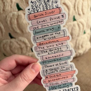 May include: A sticker in the shape of a stack of books, with titles like "Quick Silver" and "Cruel Prince." The sticker has a floral design at the top and reads "Reading Tracker 2026."
