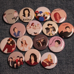 May include: A collection of round pinback buttons featuring illustrations of characters and scenes from the TV show "Friends." The buttons have various colors and designs, with some including text like "I know" and "Unagi."