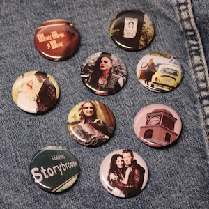 May include: Nine round buttons featuring various images from the TV show Once Upon a Time. The buttons depict characters such as Snow White, Prince Charming, Rumpelstiltskin, and the Evil Queen. Some buttons display text including "Once Upon a Time" and "Leaving Storybrooke".