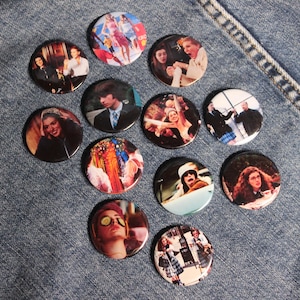 Pode incluir: Doze botões redondos com imagens de personagens do filme Meninas Malvadas. Os botões são brancos com bordas pretas e mostram imagens dos personagens em diferentes cenas do filme.