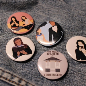 May include: Five round button pins with images from the TV show Gilmore Girls. The pins feature Lorelai and Rory Gilmore, Luke Danes, Lorelai and Sookie St. James, Lorelai Gilmore drinking coffee, and a gazebo with the text "I was meant to live in Stars Hollow".