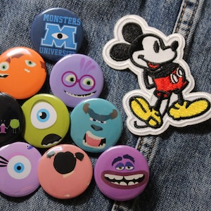 Puede incluir: Una colección de nueve parches y pines bordados de colores con personajes de la Universidad de Monstruos de Disney Pixar y Mickey Mouse. Los parches están sobre un fondo de mezclilla azul.