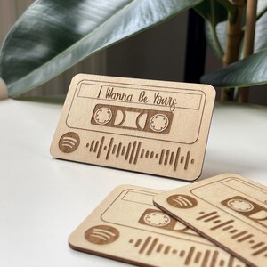 Könnte beinhalten: Helle Holz-Kassettenband-Design mit dem Text "I Wanna Be Yours" und einem Spotify-Code. Das Design umfasst eingravierte Details eines Kassettenbands und das Spotify-Logo. Mehrere dieser Artikel sind sichtbar.