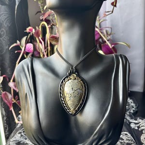 May include: A black leather cord necklace with a gold-toned pendant featuring a grey and gold pyrite stone.