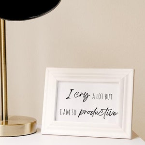 May include: White framed print with black text that reads "I cry a lot but I am so productive".