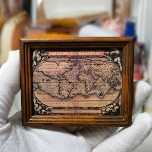 May include: A small, framed antique map of the world, featuring intricate details and text in Latin. The map is in a wooden frame, with the title "TYPVS ORBIS TERRARVM" at the top. The map's colors are muted, with shades of brown and beige.